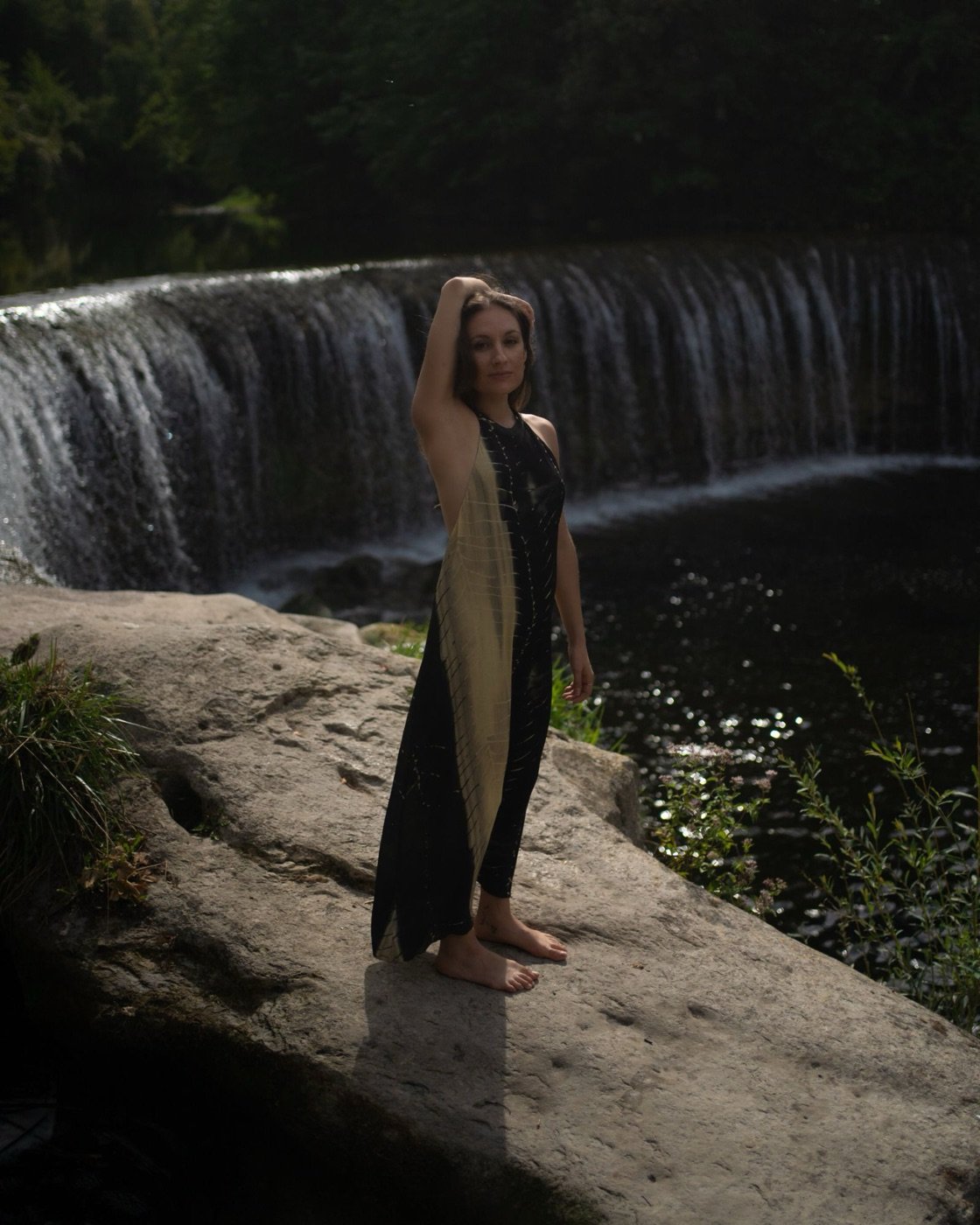 Laura Cincera standing barefoot on a rock in front of a waterfall